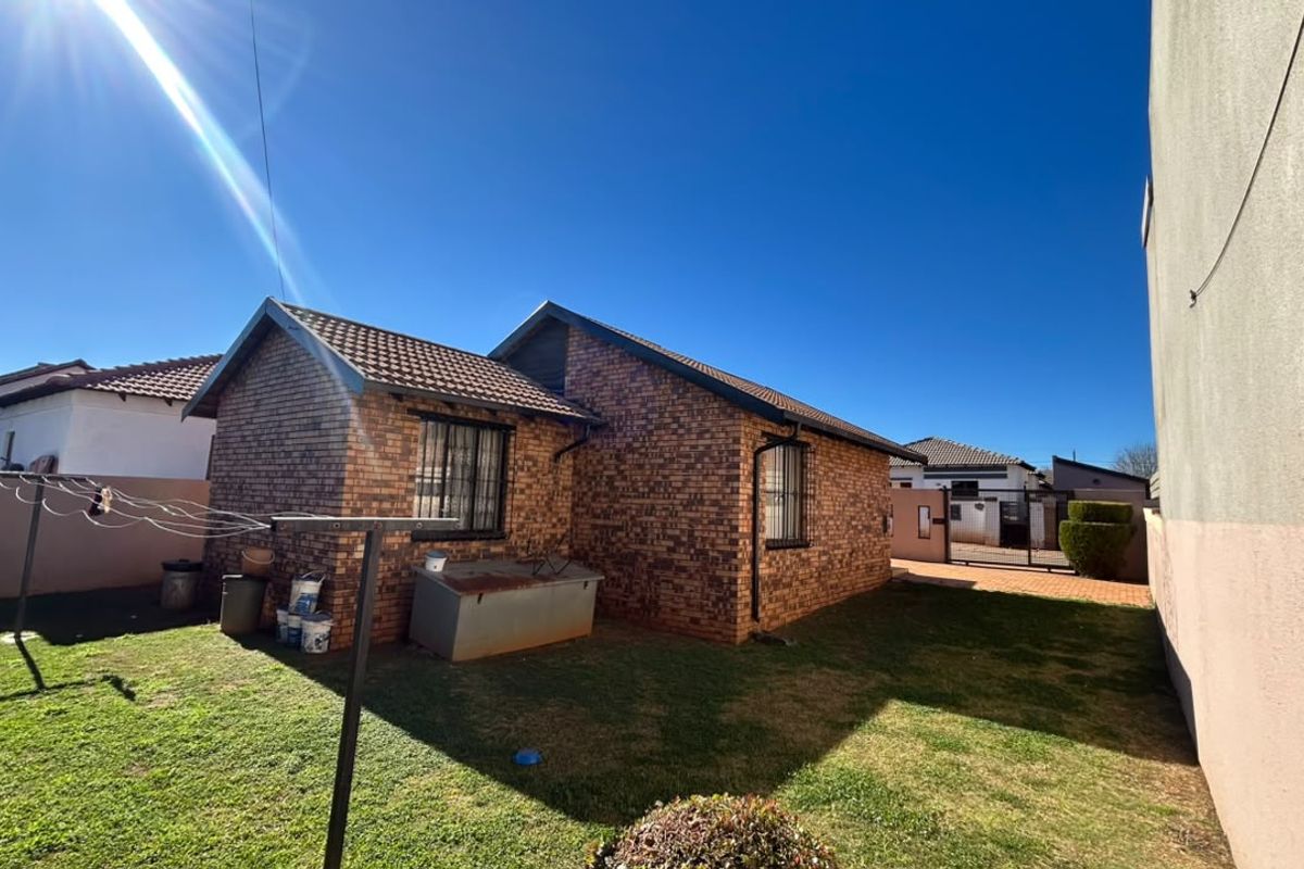 Rear view of the property featuring a face brick exterior, tiled roof, security bars on windows, and a private garden area.