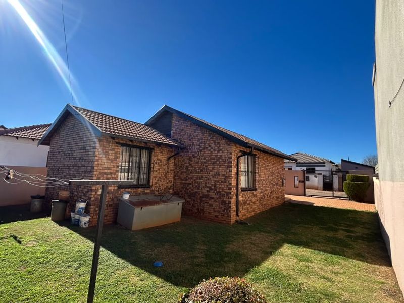 Rear view of the property featuring a face brick exterior, tiled roof, security bars on windows, and a private garden area.
