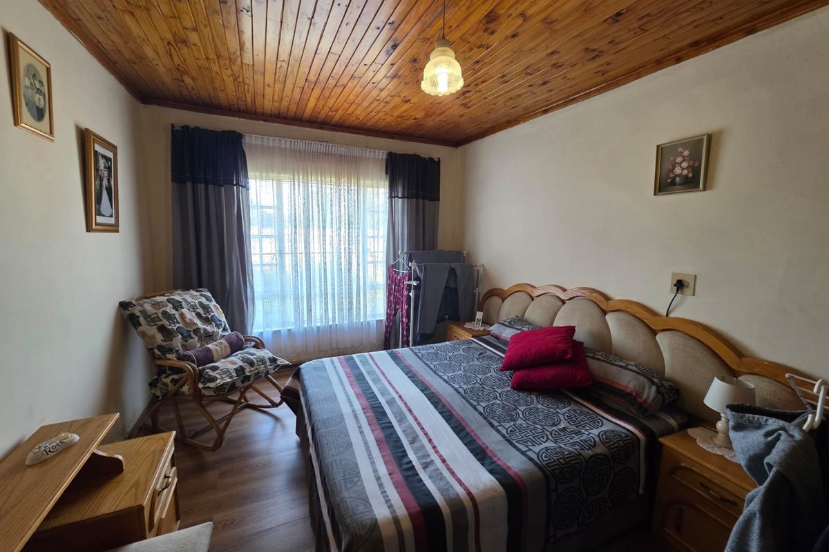A bedroom featuring a timber-clad ceiling, laminate flooring, and a built-in headboard, offering a functional space with natural light.
