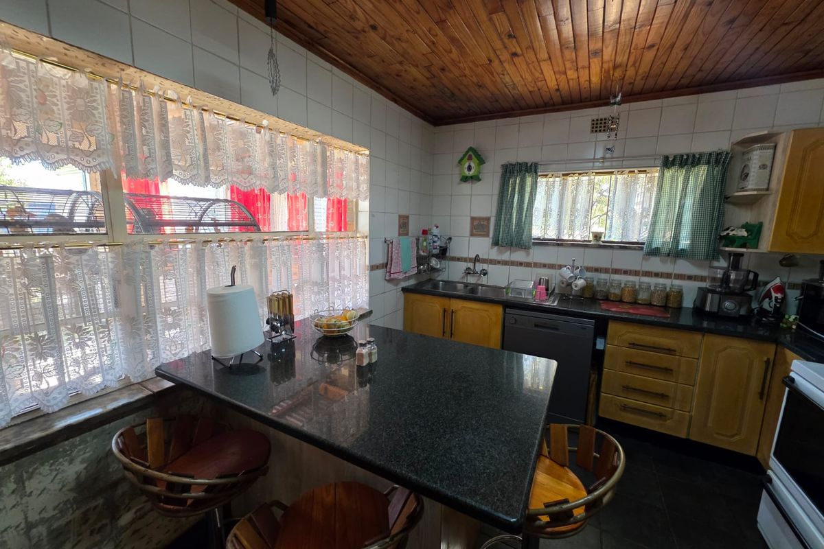 A functional kitchen featuring granite countertops, a breakfast bar, tiled splashbacks, and a distinctive timber-paneled ceiling.