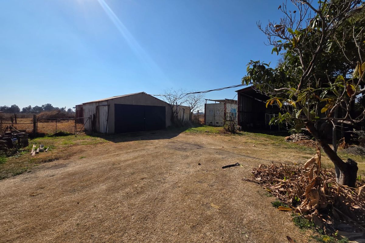 A view of the rear yard featuring a metal shed structure and open, unpaved grounds with surrounding fencing.