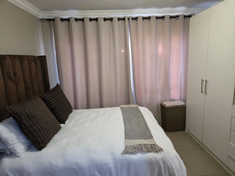 A well-maintained bedroom featuring neutral tiled flooring, crown molding, and a spacious built-in wardrobe.
