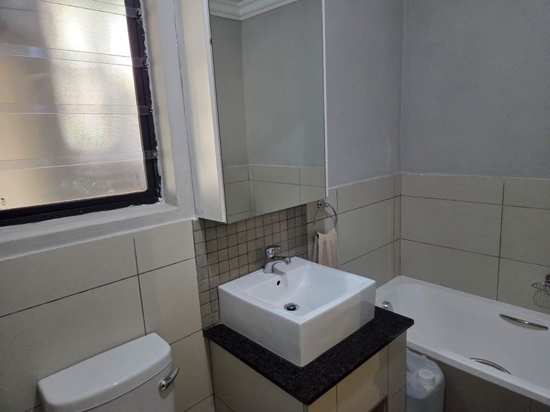 A functional bathroom featuring a vessel sink on a granite vanity, a medicine cabinet, a bathtub, and a toilet with tiled wall finishes.