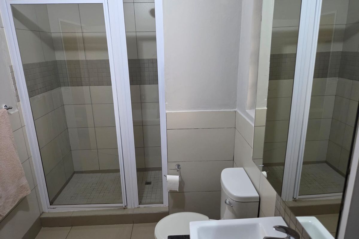 A functional bathroom featuring a walk-in shower enclosure, a vanity basin with a mixer tap, and a wall-mounted mirror.