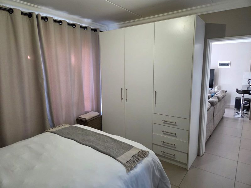 A bedroom featuring a large white built-in wardrobe with integrated drawers and tiled flooring, with a view into the adjacent living area.