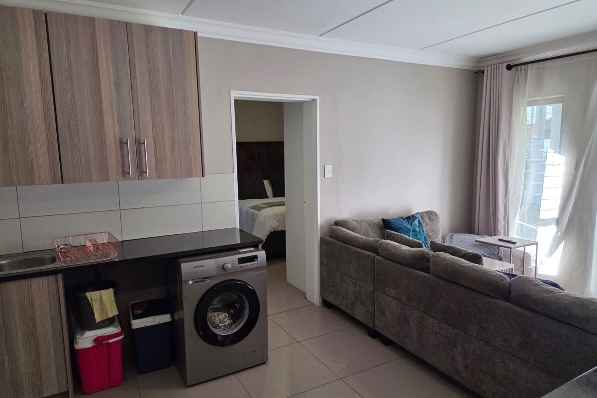 Open-plan living area featuring a compact kitchen with built-in cabinetry, granite countertops, and tiled flooring, leading to a bright lounge with balcony access.