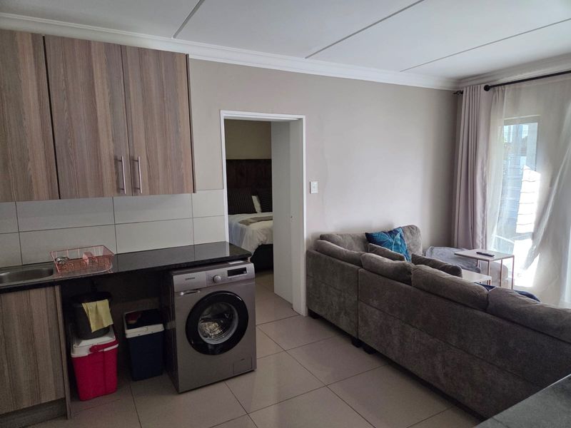Open-plan living area featuring a compact kitchen with built-in cabinetry, granite countertops, and tiled flooring, leading to a bright lounge with balcony access.