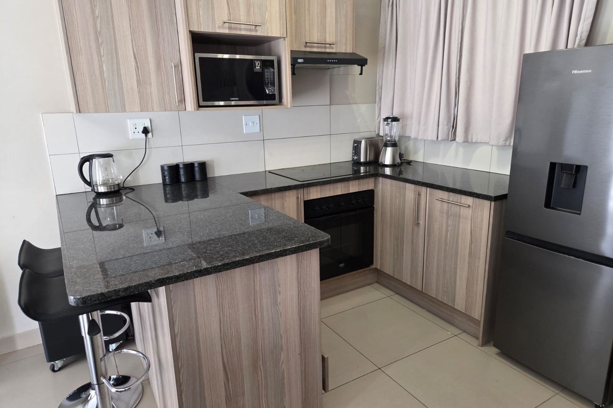 Modern kitchen featuring wood-grain cabinetry, granite countertops, integrated appliances including an oven and hob, and neutral tiled flooring.