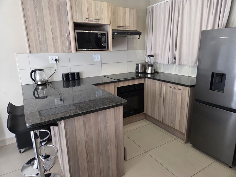 Modern kitchen featuring wood-grain cabinetry, granite countertops, integrated appliances including an oven and hob, and neutral tiled flooring.