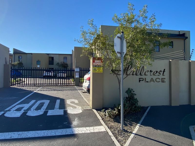 Front entrance view of Hillcrest Place apartment complex featuring secure gated access, paved driveway, and perimeter electric fencing.