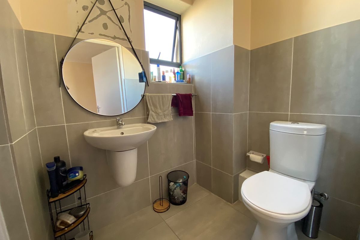 A functional bathroom featuring a pedestal washbasin, toilet, and neutral wall and floor tiling with a window for natural light.