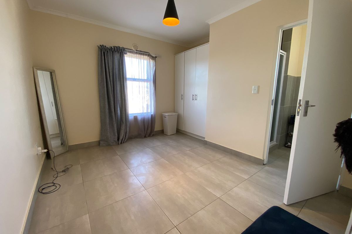 A bright, empty bedroom featuring neutral tiled flooring, a built-in wardrobe, and direct access to an en-suite bathroom.