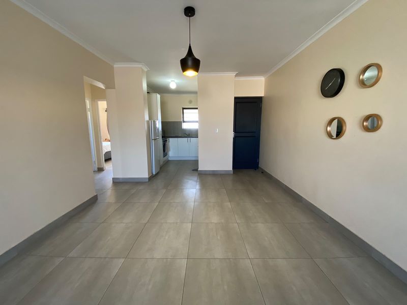 An open-plan living and kitchen area featuring neutral tiled flooring, modern pendant lighting, and clean, functional kitchen cabinetry.