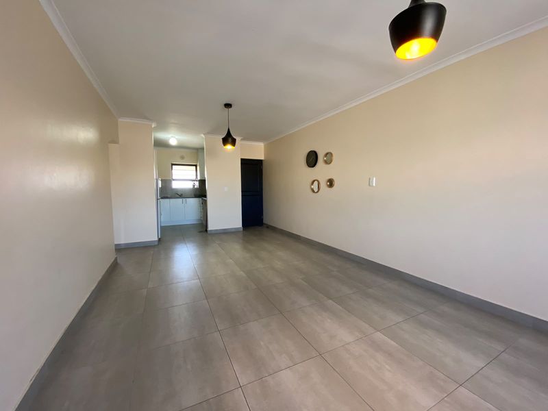 Spacious open-plan living area featuring neutral tiled flooring, modern pendant lighting, and a view through to the functional kitchen space.