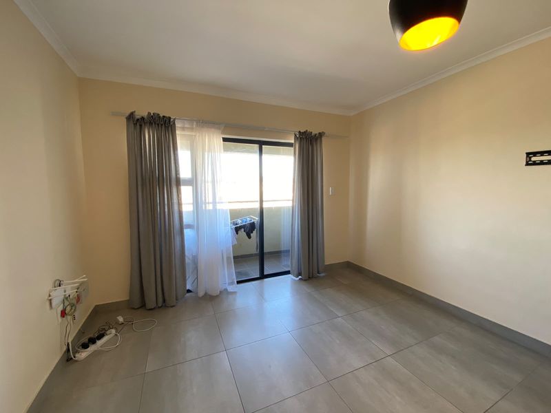 A bright, empty living room featuring large sliding glass doors leading to a balcony, neutral tiled flooring, and clean wall finishes.
