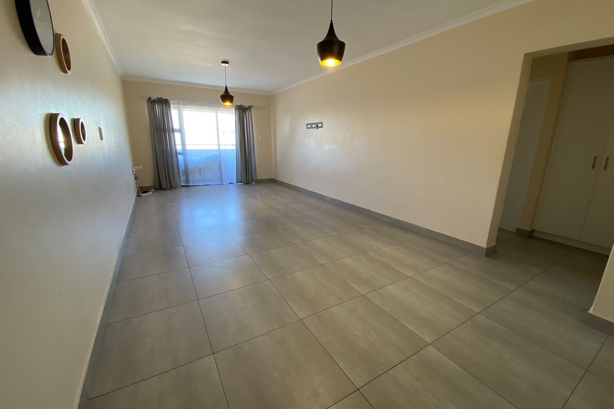A spacious, empty living room featuring neutral tiled flooring, modern pendant lighting, and a sliding glass door leading to an outdoor area.