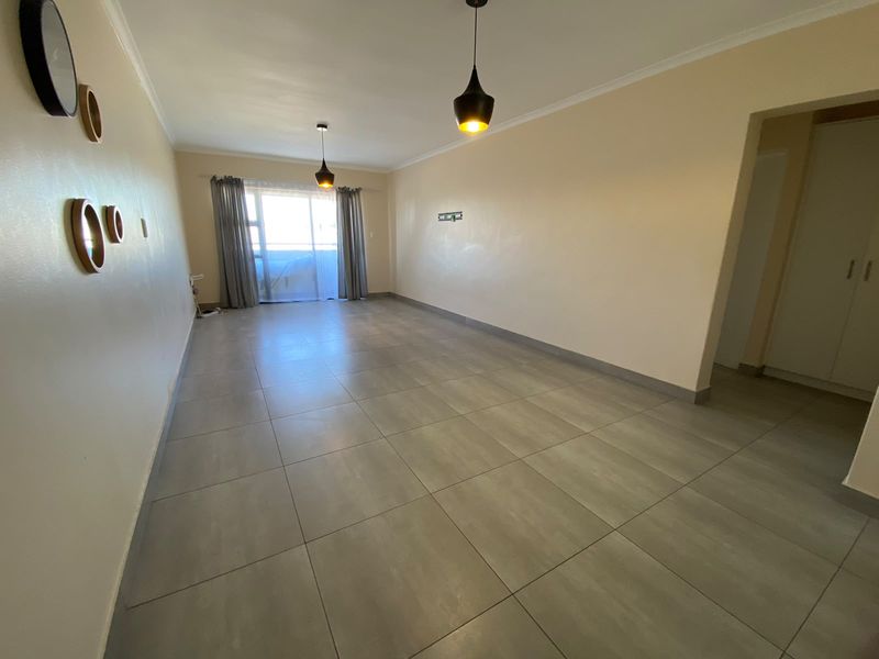 A spacious, empty living room featuring neutral tiled flooring, modern pendant lighting, and a sliding glass door leading to an outdoor area.