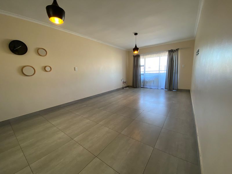 A spacious, empty living room featuring neutral tiled flooring, modern pendant lighting, and a sliding glass door leading to an outdoor area.