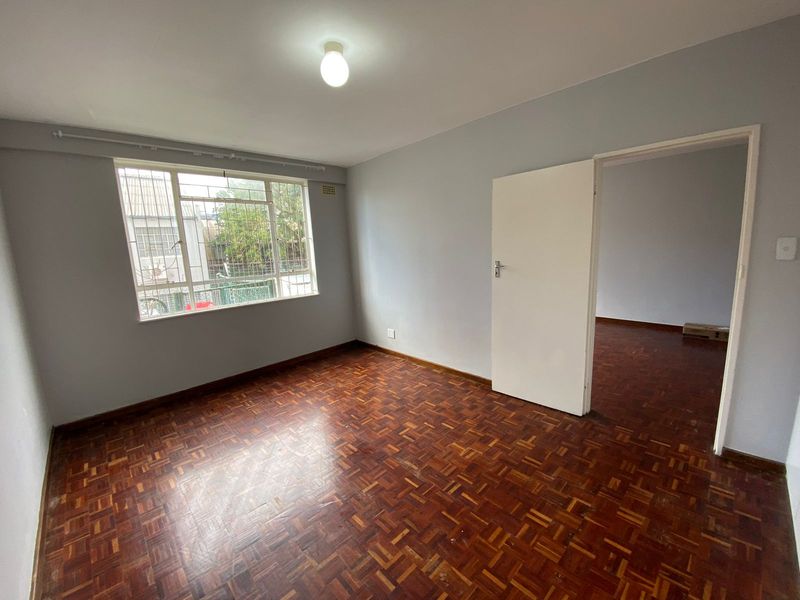 An empty bedroom featuring original parquet flooring, neutral wall paint, and a window fitted with security bars.
