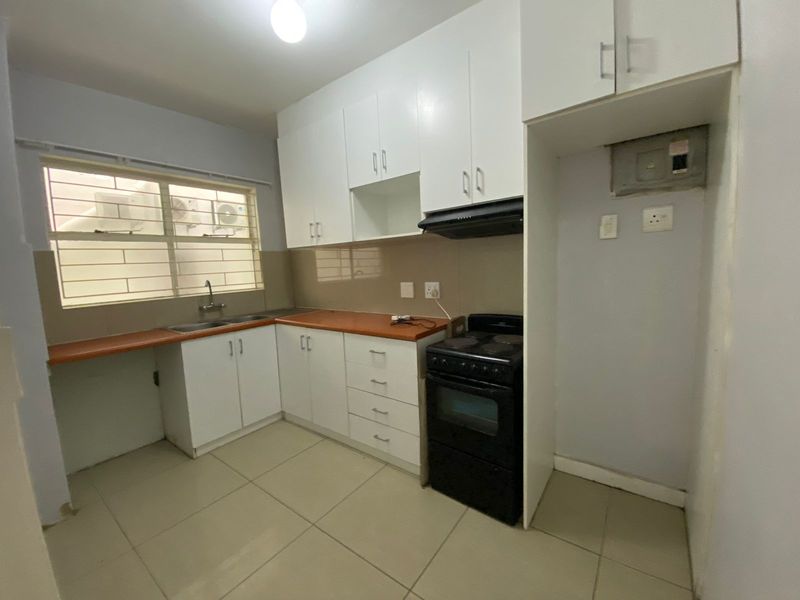 A functional kitchen featuring white cabinetry, a laminate countertop, tiled flooring, and a dedicated space for a freestanding stove and refrigerator.