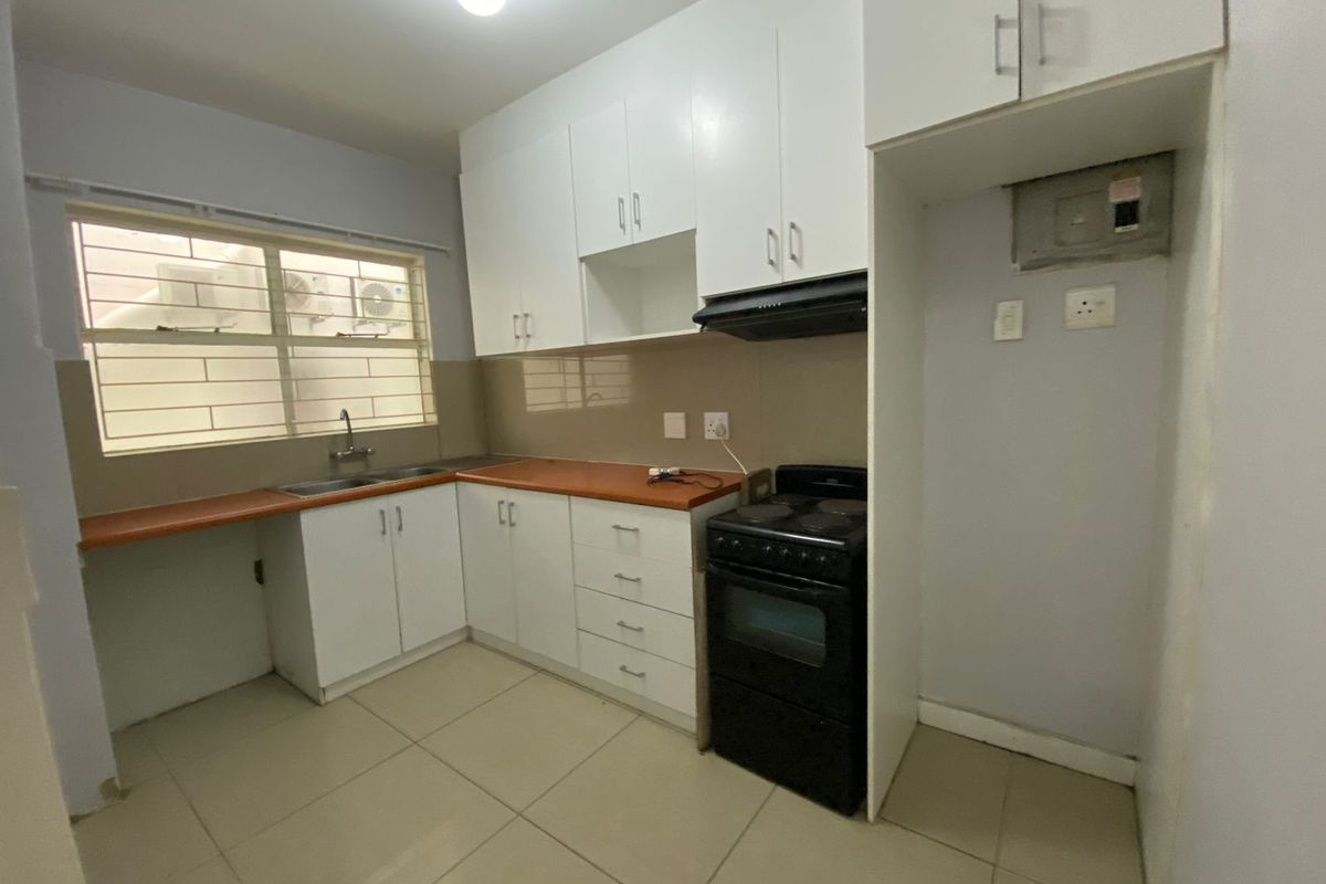 A functional kitchen featuring white cabinetry, a laminate countertop, tiled flooring, and a dedicated space for a freestanding stove and refrigerator.