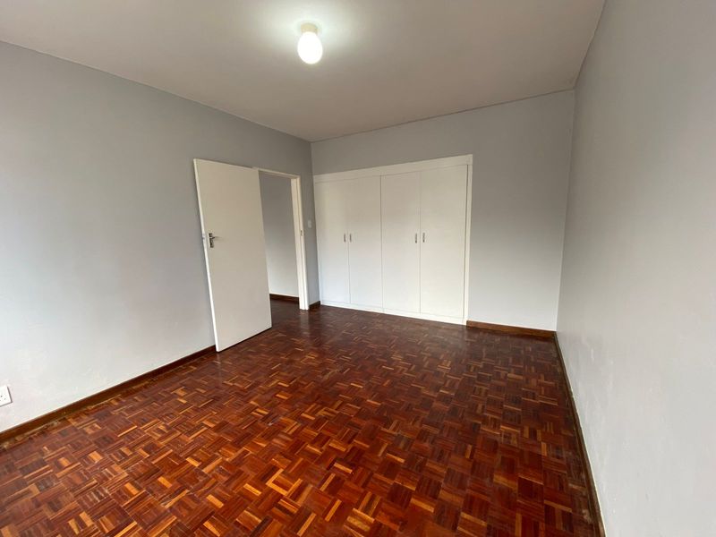 A bright, empty bedroom featuring classic parquet flooring and ample built-in cupboard storage space.