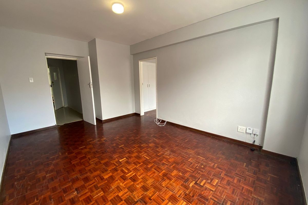 An empty living room featuring traditional parquet flooring, neutral walls, and access to adjacent rooms through internal doorways.