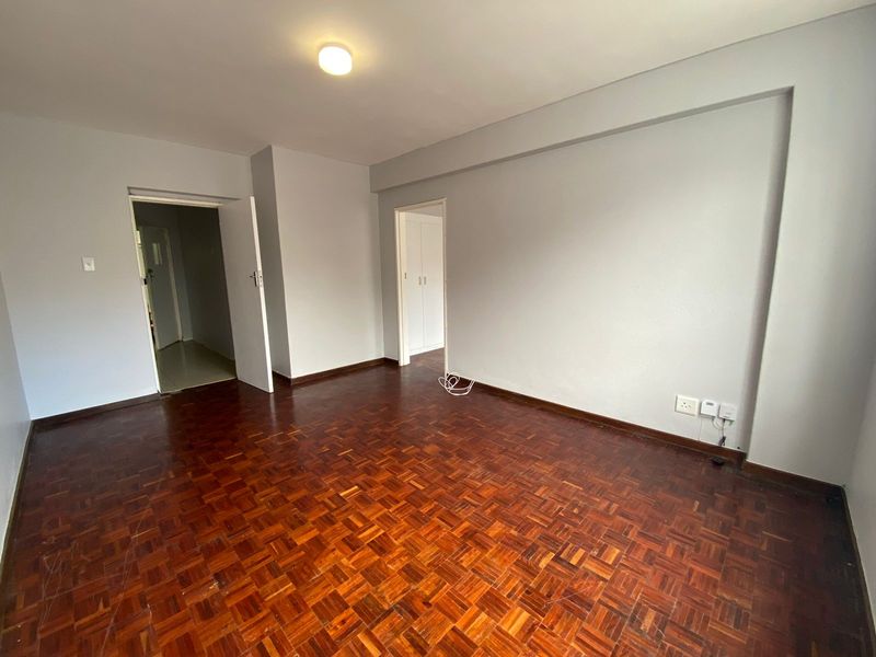 An empty living room featuring traditional parquet flooring, neutral walls, and access to adjacent rooms through internal doorways.