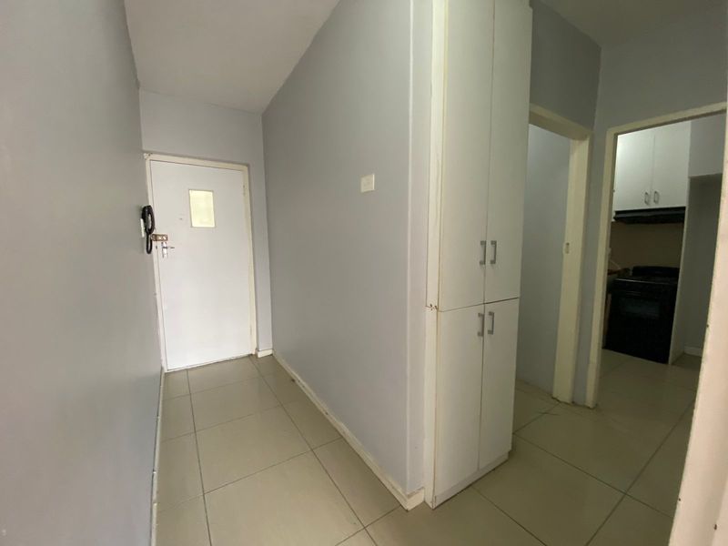 A functional entrance hallway featuring tiled flooring, a built-in storage cupboard, and an intercom system, providing access to the kitchen area.