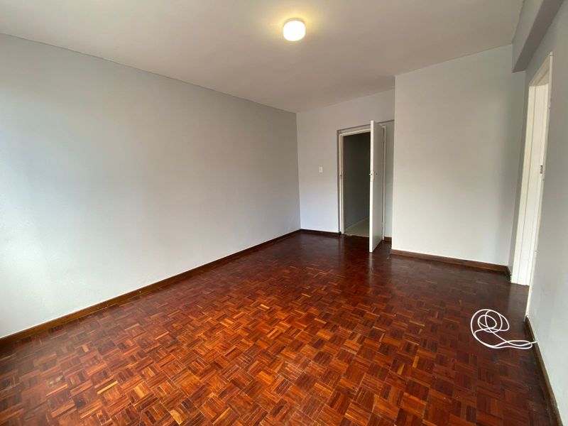 An empty bedroom featuring well-maintained parquet flooring and neutral wall finishes, providing a blank canvas for interior design.