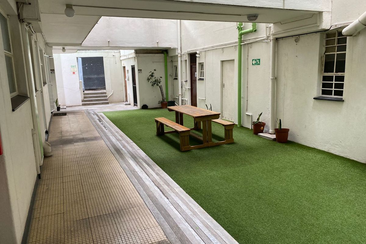 A communal courtyard area featuring artificial turf, tiled walkways, and exposed utility infrastructure, providing a functional outdoor space for residents.