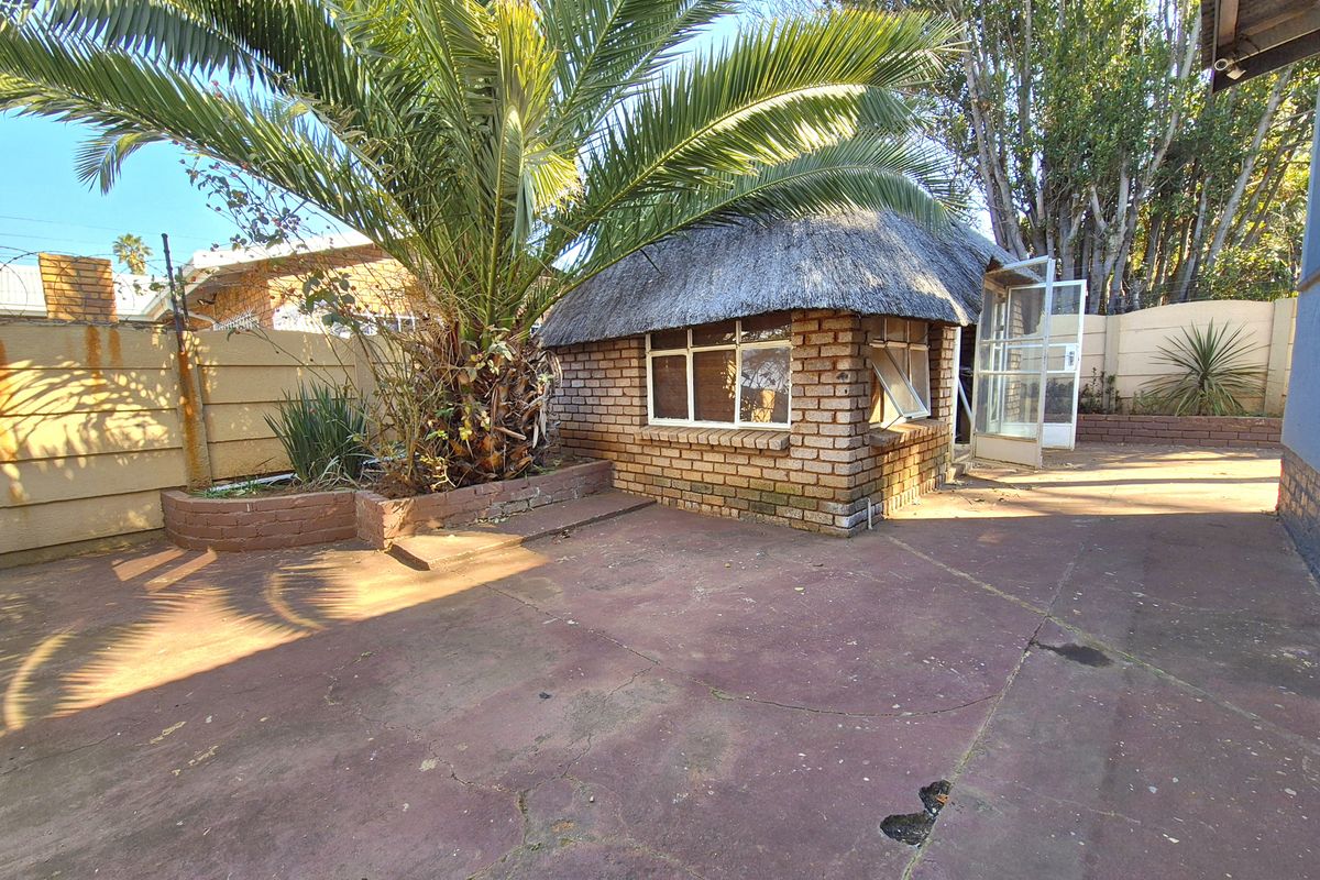 Rear garden area featuring a small thatch-roofed structure, concrete paving, and a raised brick planter against a boundary wall.