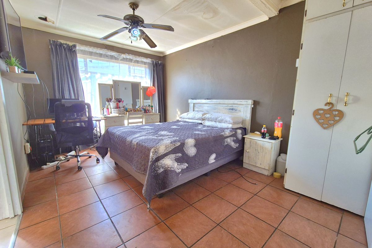 A bedroom featuring tiled flooring, built-in cupboards, and a ceiling fan, currently showing signs of wear and ceiling water damage.