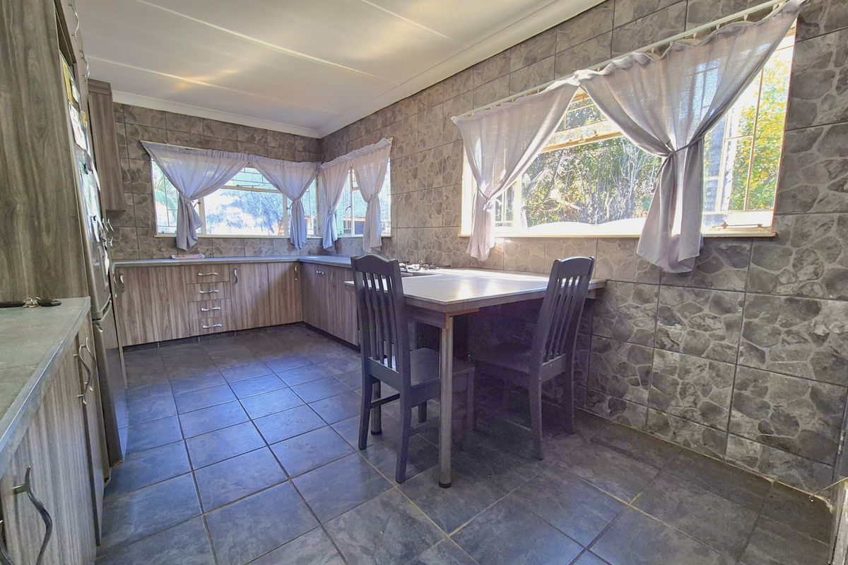 A functional kitchen featuring tiled walls and flooring, laminate cabinetry, and ample natural light through multiple windows with security bars.