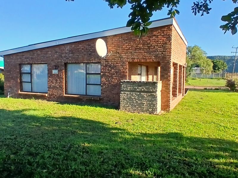 A single-story face brick house featuring a mono-pitch roof and aluminium window frames, set within a spacious grassed yard.
