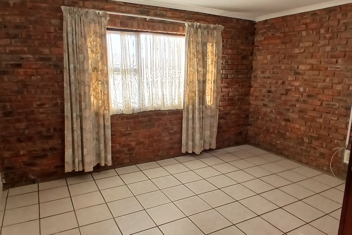 A vacant bedroom featuring exposed brick walls, ceramic floor tiling, and wooden wall paneling, offering a rustic aesthetic ready for personalization.