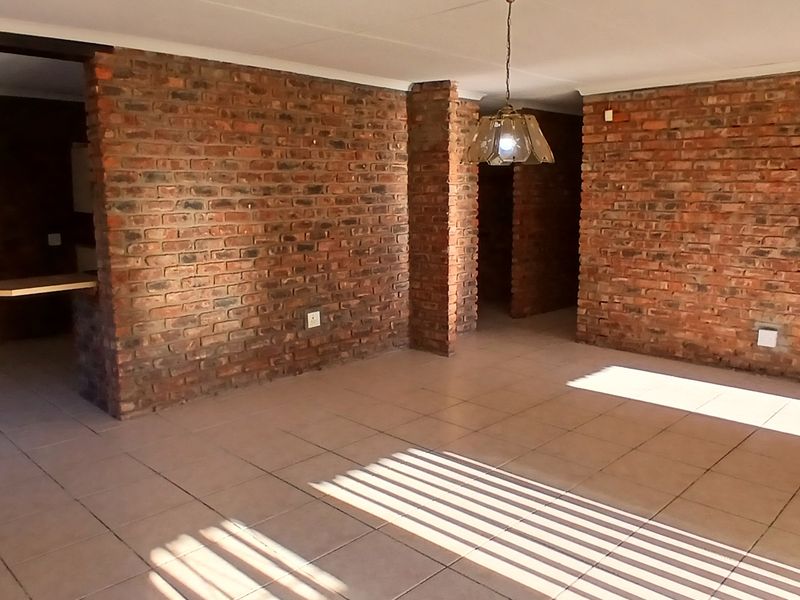 Spacious living area featuring rustic exposed brick walls, neutral tiled flooring, and a built-in breakfast bar, offering a versatile open-plan layout.