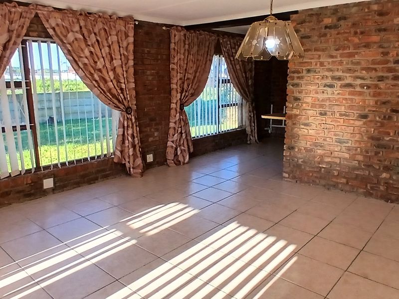 Spacious living area featuring exposed brick walls, ceramic floor tiling, and large windows with vertical blinds, offering a neutral canvas for interior design.