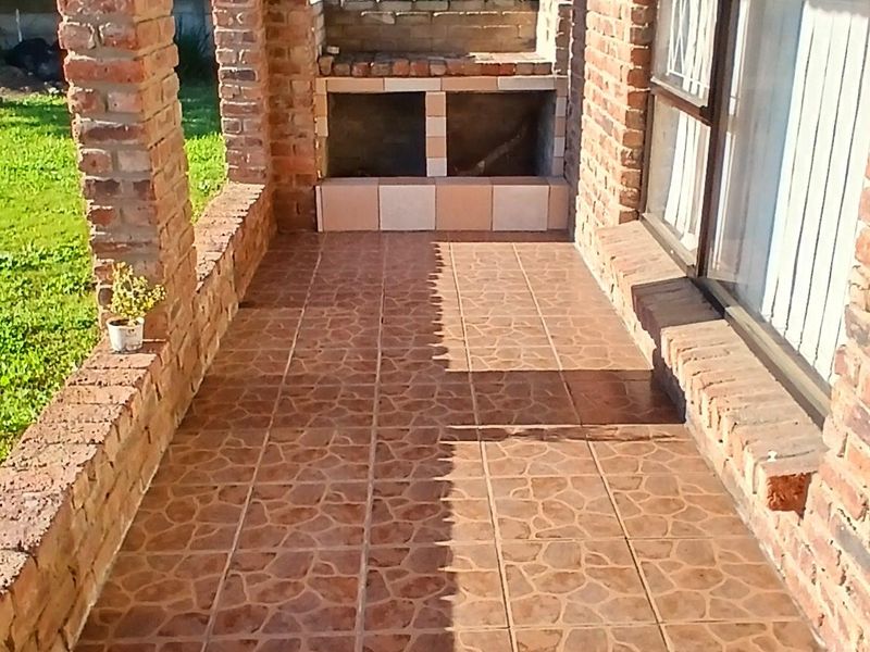 Covered patio area featuring exposed brick pillars, tiled flooring, and a built-in braai, overlooking the garden.