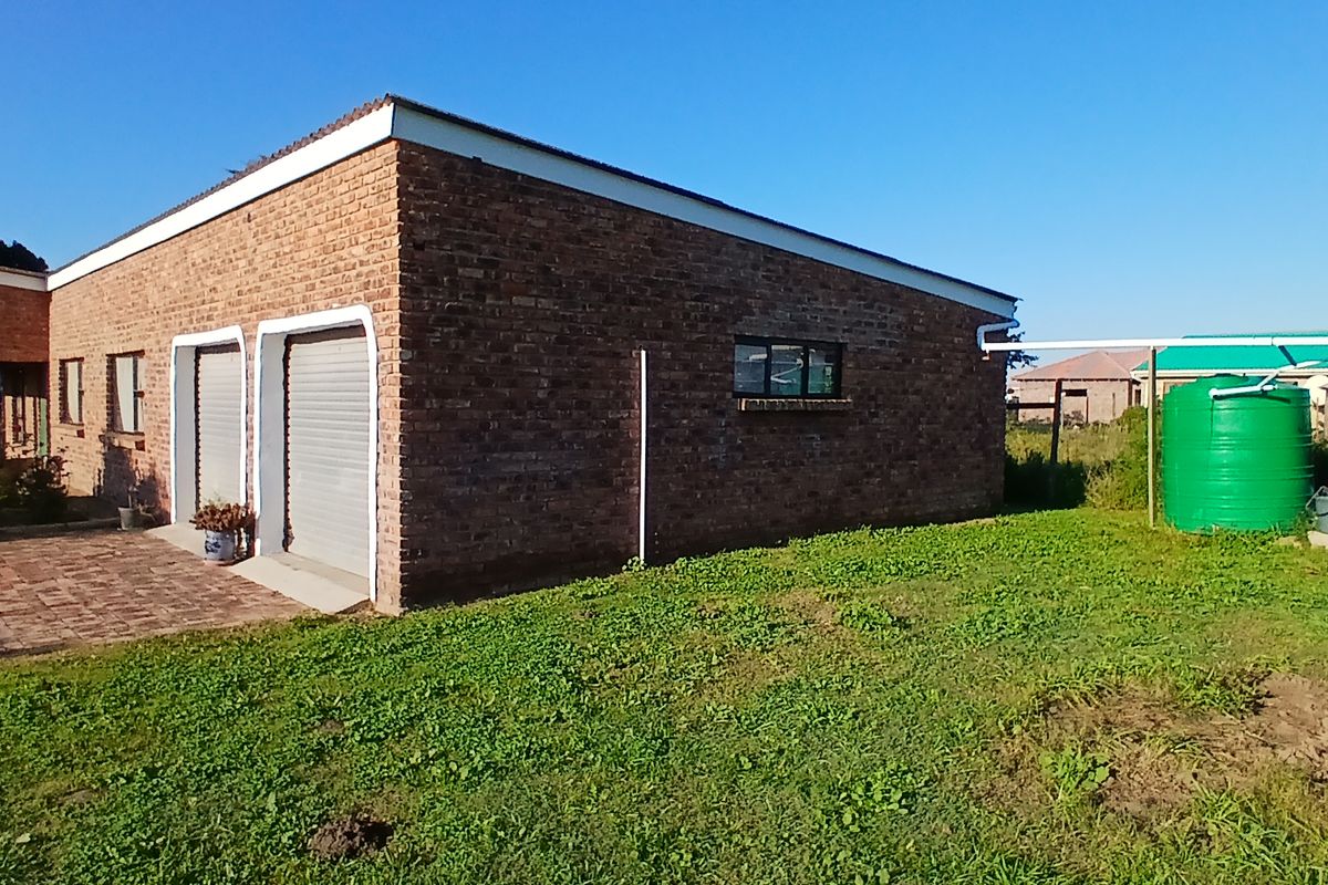 Rear view of a face brick house featuring a double garage with roller shutter doors, paved driveway, and external water storage tanks.