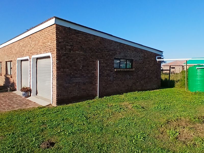 Rear view of a face brick house featuring a double garage with roller shutter doors, paved driveway, and external water storage tanks.