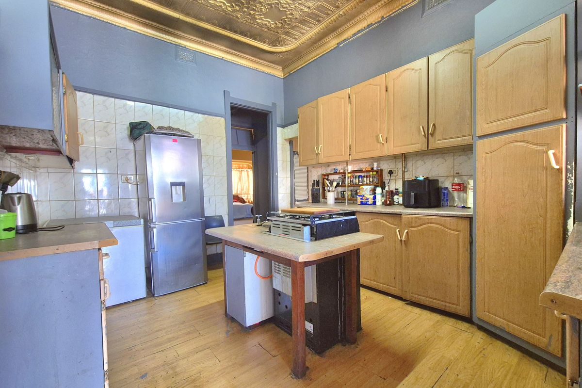 A dated kitchen featuring timber cabinetry, tiled splashbacks, and a distinctive pressed metal ceiling, offering significant potential for a modern renovation.