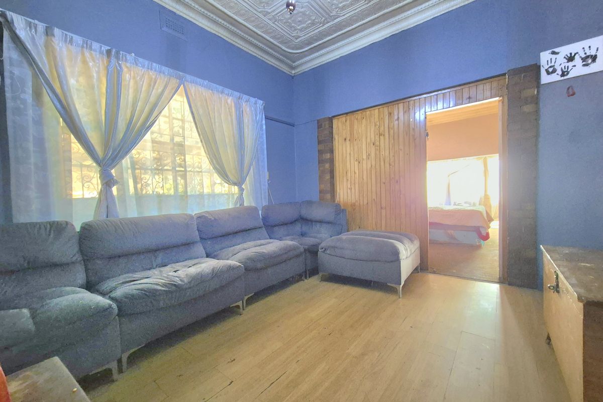 A living room featuring original pressed metal ceilings, timber flooring, and timber wall paneling, offering a classic character aesthetic in need of cosmetic updates.