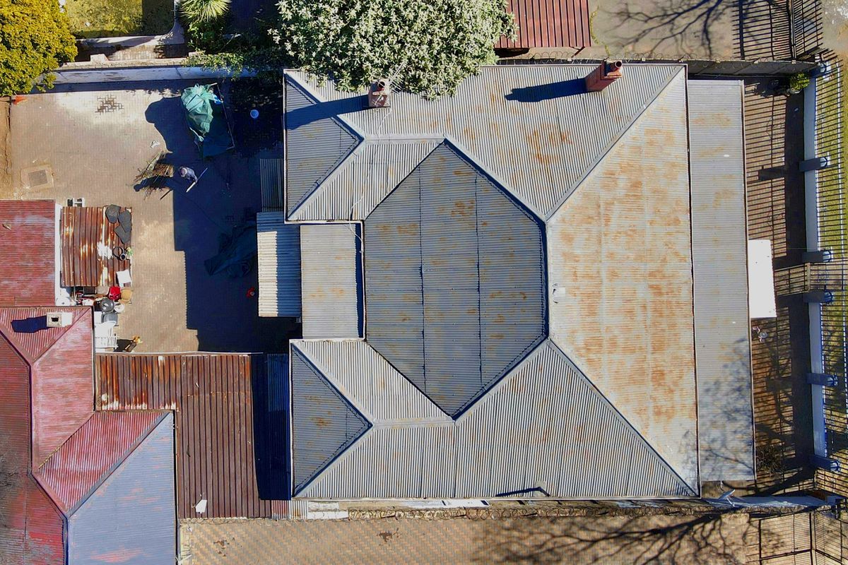 Aerial view of the property showing the roof structure, paved driveway, and perimeter fencing, with visible signs of surface rust on the metal roofing.