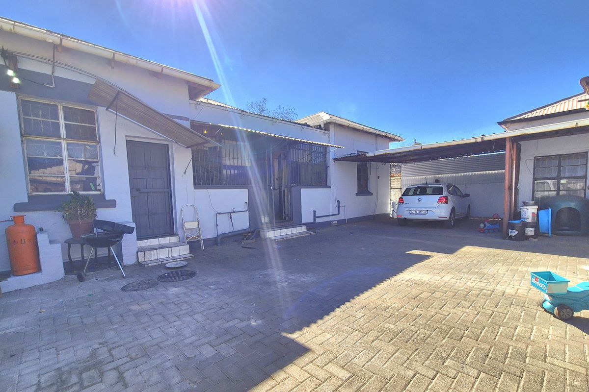 Rear exterior view of the property featuring a paved driveway, a covered carport area, and security bars on the windows.