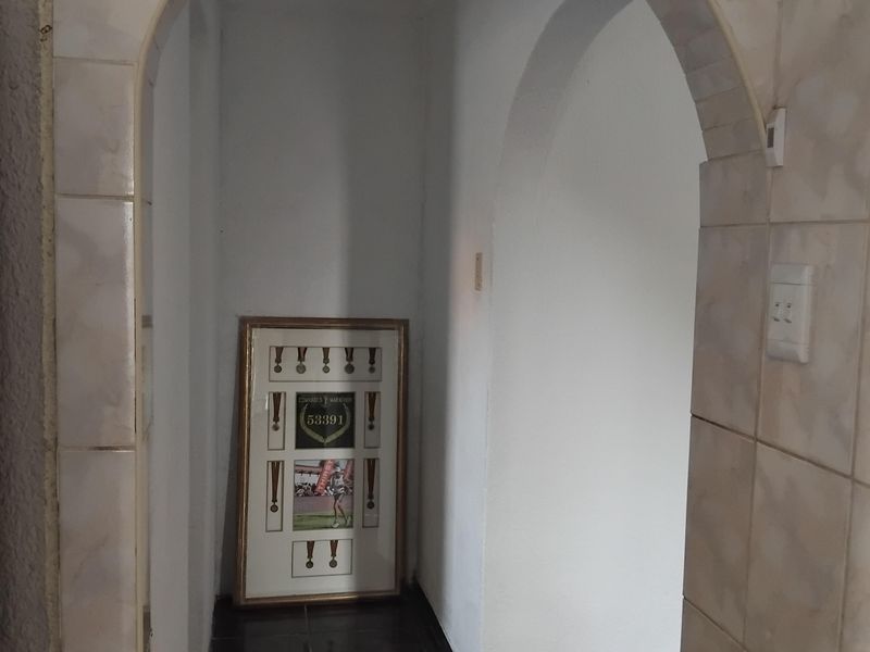 A narrow hallway featuring an arched entryway, tiled walls, and dark floor tiles, presenting a dated aesthetic in need of modernization.
