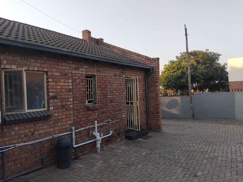 Rear view of a face brick flat featuring a paved courtyard area, security gates, and external plumbing infrastructure.