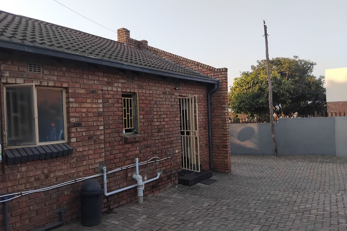 Rear view of a face brick flat featuring a paved courtyard area, security gates, and external plumbing infrastructure.
