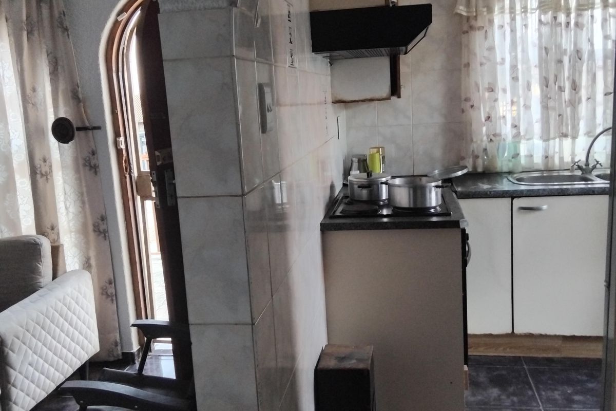 Compact kitchen featuring built-in cabinetry, a hob with extractor fan, and a stainless steel sink, connected to the living area via an arched doorway.