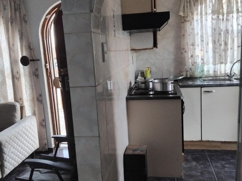 Compact kitchen featuring built-in cabinetry, a hob with extractor fan, and a stainless steel sink, connected to the living area via an arched doorway.